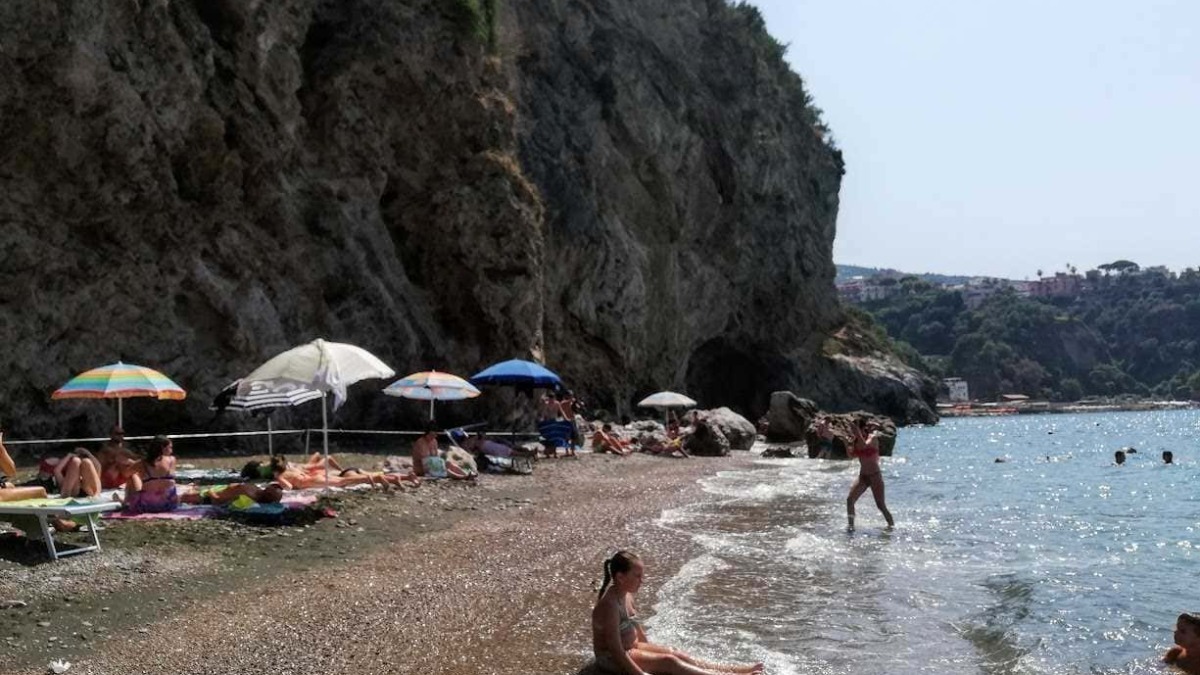 Spiaggia con ciottoli e ombrelloni colorati, scogli e mare cristallino al mare, persone che si rilassano e nuotano, paesaggio naturale e relax estivo, località balneare in Italia.