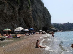 Spiaggia con ciottoli e ombrelloni colorati, scogli e mare cristallino al mare, persone che si rilassano e nuotano, paesaggio naturale e relax estivo, località balneare in Italia.