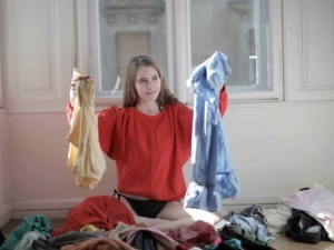 Stress da lavatrice e disordine in casa, giovane donna con maglietta rossa, che cerca di mettere in ordine i vestiti, in una stanza luminosa con grandi finestre.