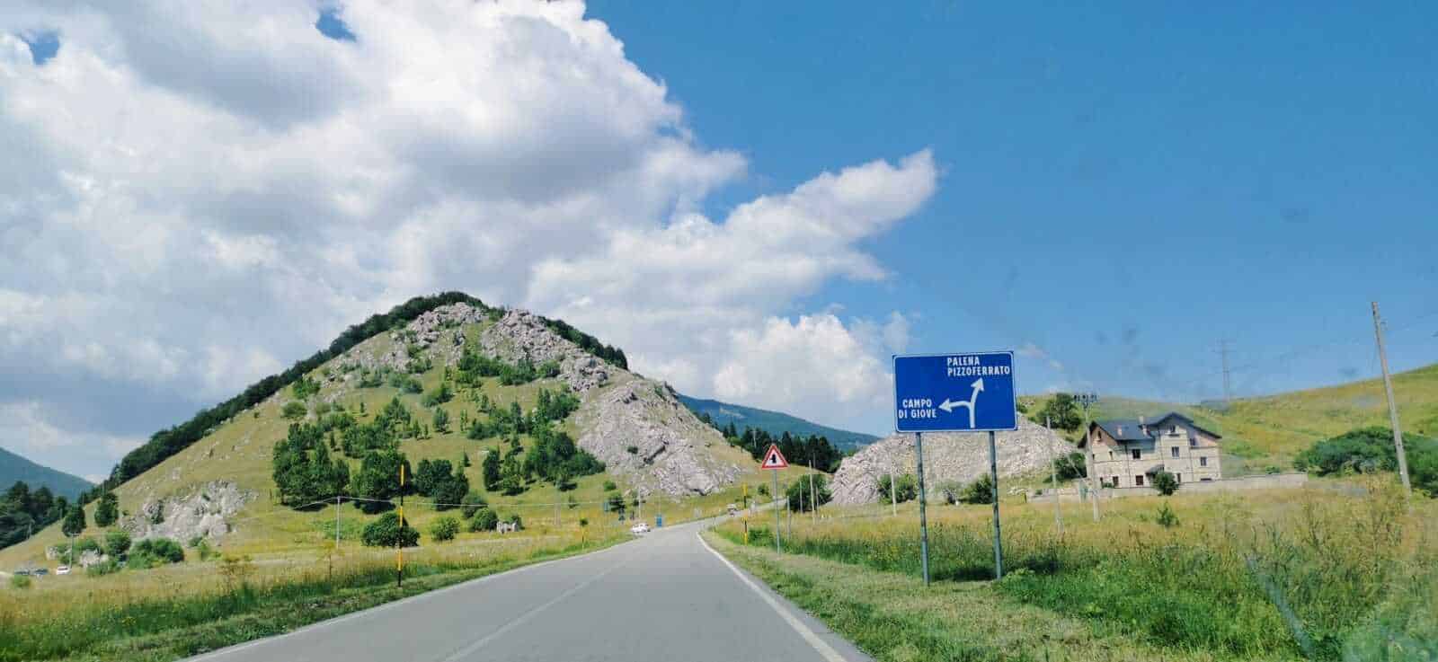 Parco Nazionale della Majella, 12 attrazioni in Abruzzo 2 Montagna verde con strada di campagna e segnaletica stradale in Italia, paesaggio naturale e cielo azzurro.