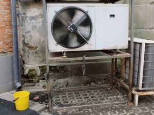 Climatizzatore esterno su supporto metallico, installazione in ambiente urbano, con scatola di corrente e tubazioni.