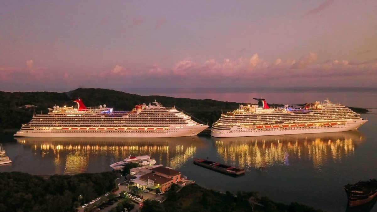 Gemelli di navi da crociera illuminati di sera in un porto marina, riflessi sull'acqua, paesaggio marittimo, vacanze, turismo, crociere di lusso, vista aerea, atmosfera rilassante, scena notturna.