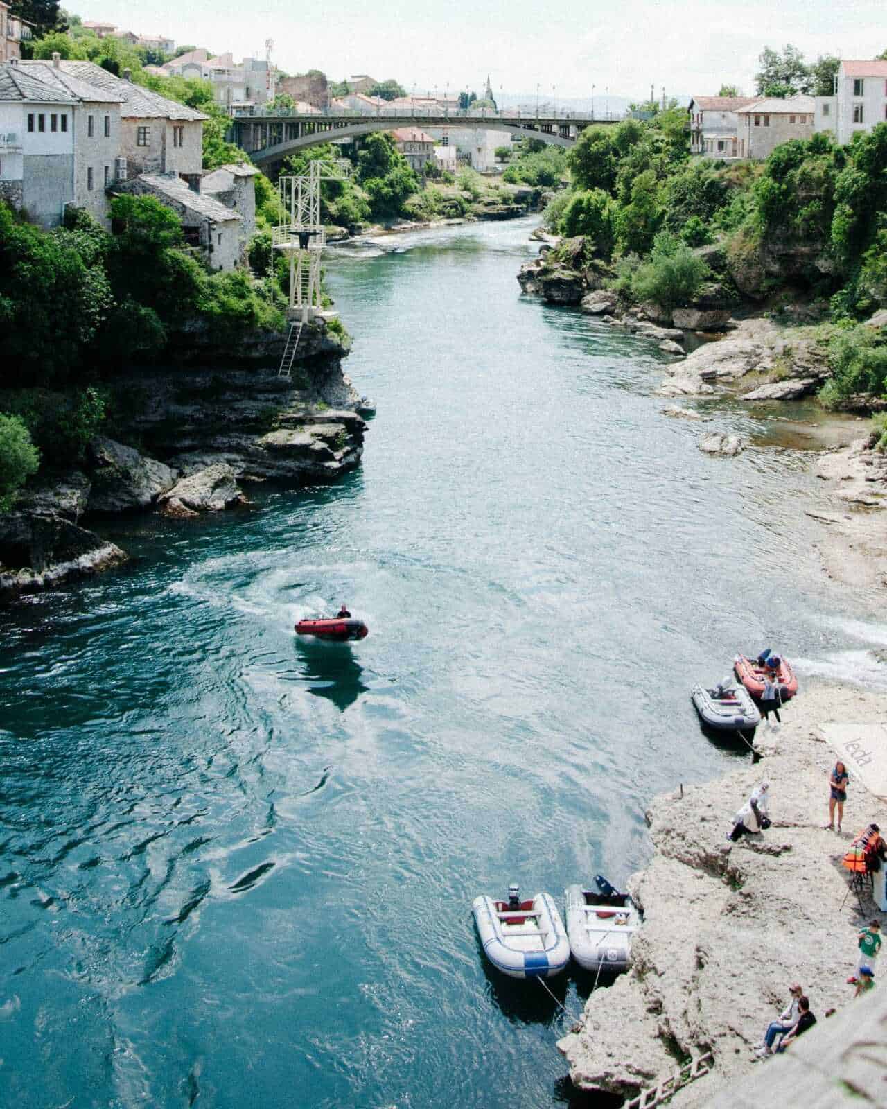 Lago Ilissos a Potenza, con barche in acqua e falesia con persone che si rilassano, circondato da case e vegetazione, in una giornata di relax e attività all'aperto nel cuore della città.