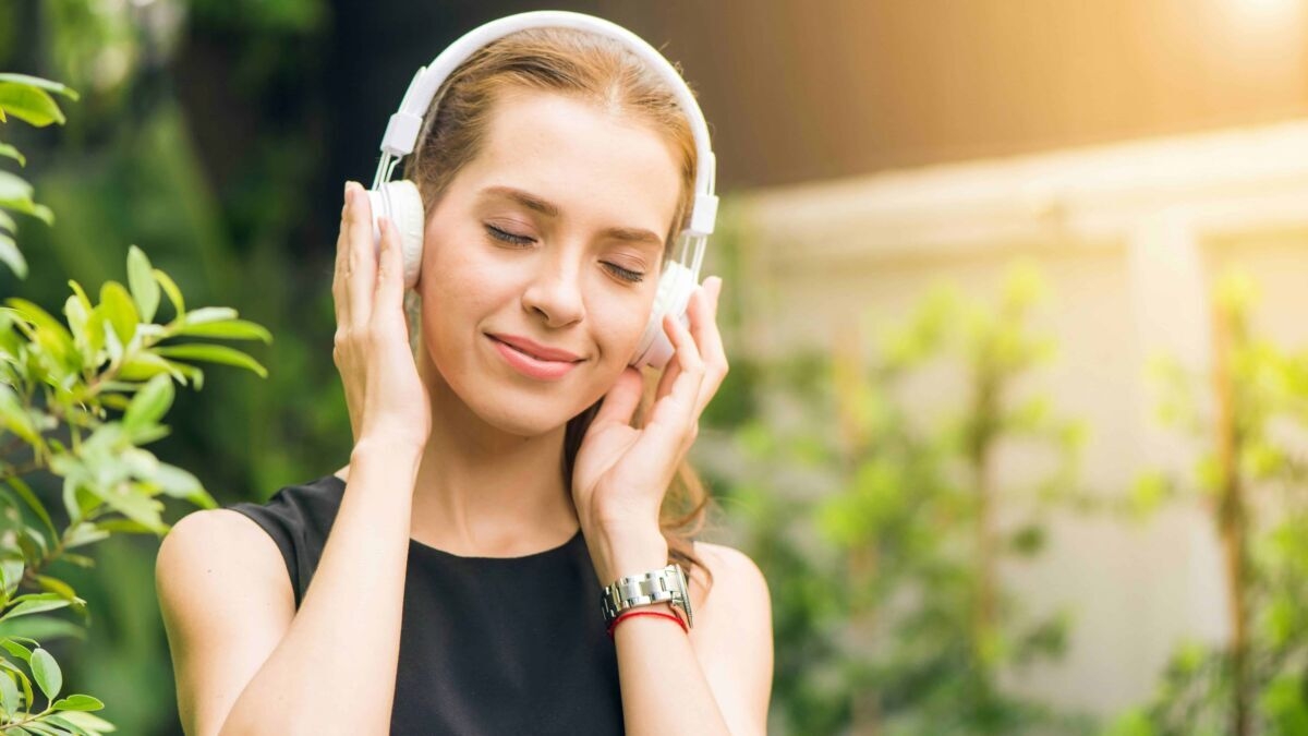 Musica e relax all'aperto: donna che ascolta musica con cuffie in natura, ambiente verde e solare, perfetto esempio di benessere e ascolto musica relax all'aperto.