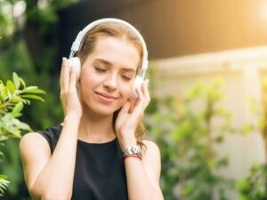 Musica e relax all'aperto: donna che ascolta musica con cuffie in natura, ambiente verde e solare, perfetto esempio di benessere e ascolto musica relax all'aperto.