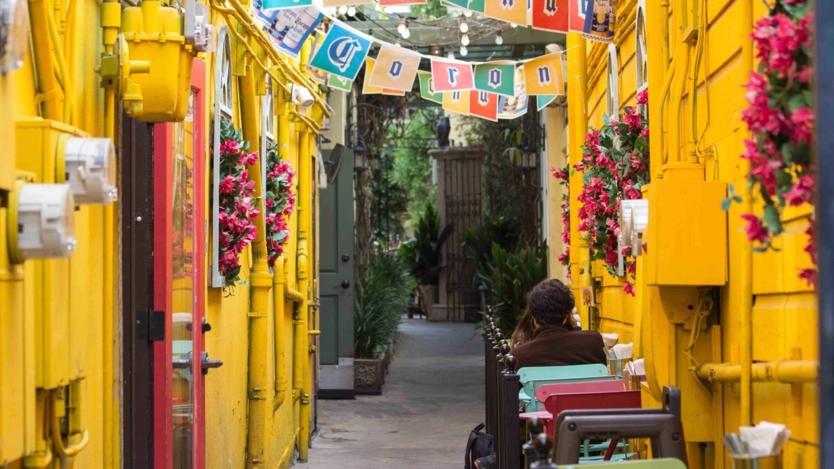 Colorato vicolo di strada con pareti gialle, decorato con fiori e festoni, atmosfera allegra e vivace, ideale per fotografie di viaggi, cultura e street art in contesti urbani italiani.