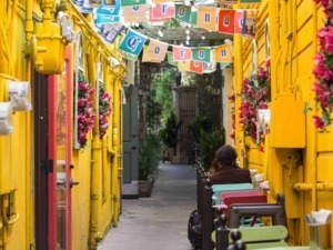 Colorato vicolo di strada con pareti gialle, decorato con fiori e festoni, atmosfera allegra e vivace, ideale per fotografie di viaggi, cultura e street art in contesti urbani italiani.