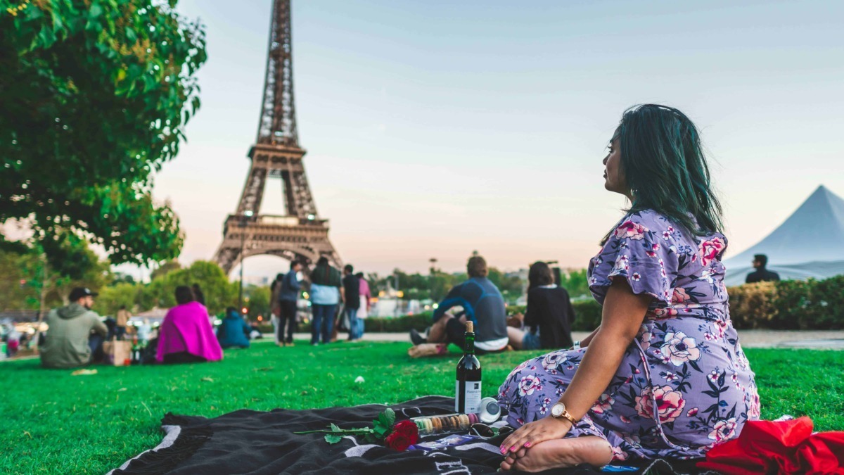 Vista della Torre Eiffel di Parigi al tramonto con persone che fanno un picnic nel parco, ambiente romantico e turistico, ideale per contenuti su viaggio, Francia e cultura europea.