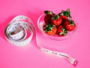 Fette di plastica e ciotola di fragole fresche con nastro da misurazione su sfondo rosa.
