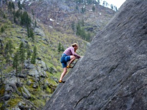 Escursionista che arrampica su una parete di roccia in una zona montana selvaggia durante una giornata di primavera.