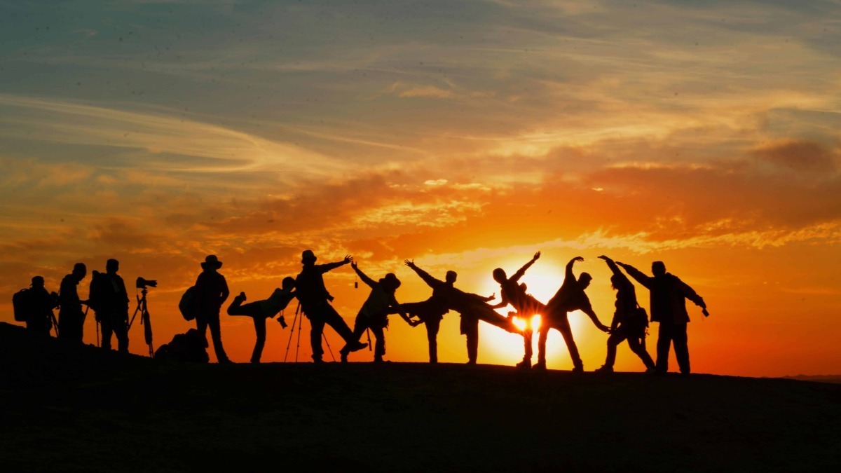 Silhouette di un gruppo di amici che si diverte al tramonto, scattando foto e condividendo momenti di gioia all'aperto, perfetti per blog di viaggi e avventure outdoor.