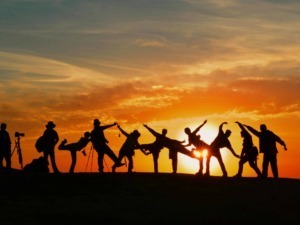Silhouette di un gruppo di amici che si diverte al tramonto, scattando foto e condividendo momenti di gioia all'aperto, perfetti per blog di viaggi e avventure outdoor.