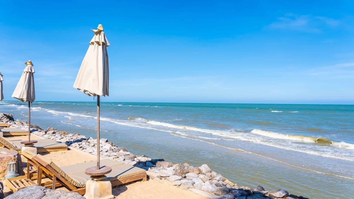 Parapioggia sulla spiaggia con ombrelloni e lettini in stile riposo estivo, mare blu e cielo sereno, ideale per relax, vacanze e gite sulla costa.