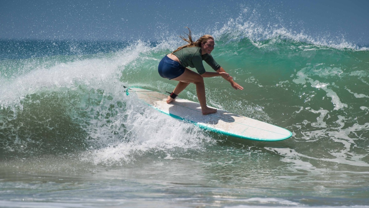 Praticante di surf femminile che cavalca un'onda in mare aperto, mostrando abilità e equilibrio sulla tavola. Scene di surf sportivo e avventura acquatica per appassionati di mare e sport estremi.