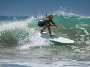 Praticante di surf femminile che cavalca un'onda in mare aperto, mostrando abilità e equilibrio sulla tavola. Scene di surf sportivo e avventura acquatica per appassionati di mare e sport estremi.