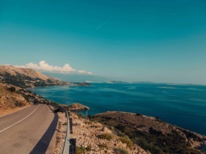 Tragitto costiero panoramico con vista mare e colline, strada asfaltata con guardrail, paesaggio mediterraneo, viaggio in auto lungo la costa, bellezza naturale, scenari di mare e montagna in Italia.