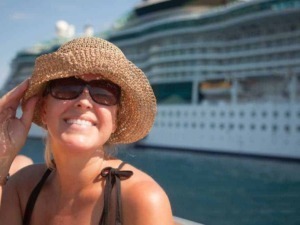 Sorriso di una donna con cappello di paglia e occhiali da sole in porto, con una grande nave da crociera sullo sfondo, atmosfera estiva e relax.