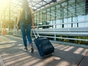 Bagaglio a mano con rotelle all'aeroporto, giovane donna con zaino in spalla e trolley in mano, viaggio e turismo, moderna struttura aeroportuale in background.