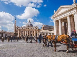 Passeggio in Piazza San Pietro a Roma, con la Basilica di San Pietro e il colonnato imponenti nello sfondo, in una giornata soleggiata con nuvole leggere nel cielo.