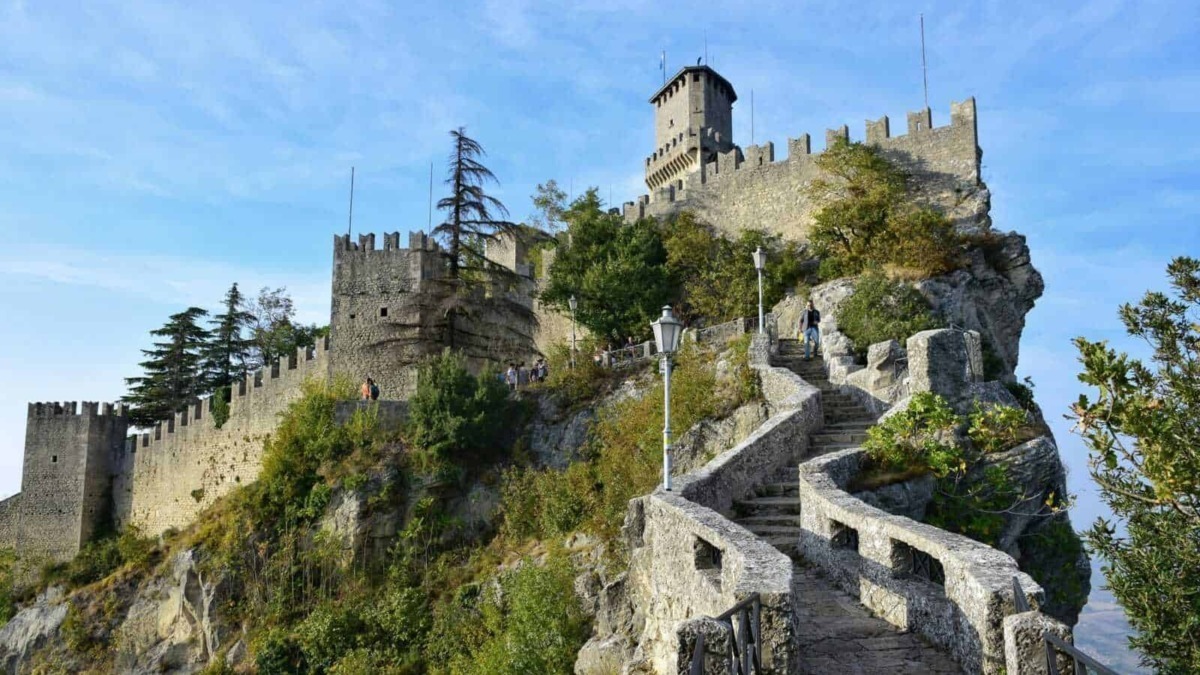 Castello medievale su scogliera con scale in pietra e vegetazione, panorama storico e turistico, destinazione da visitare in Italia, fortezza affascinante e panorami mozzafiato.