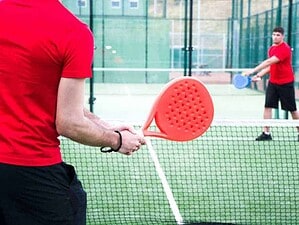 Ragazzo che si allena a padel sulla pista in outdoor con attrezzature sportive di gioco.