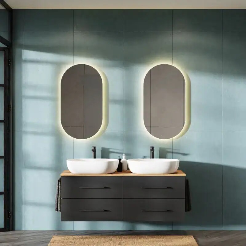 Lavabo duo con specchi ovali a illuminazione retro a parete in bagno moderno con mobile sospeso nero e pareti azzurro pastello.