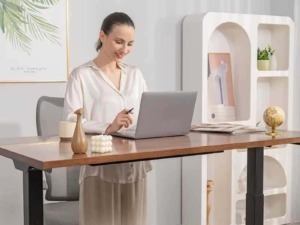 Schermata di donna sorridente mentre lavora al computer in un ambiente elegante e minimalista con decorazioni moderne e piante verde chiaro.