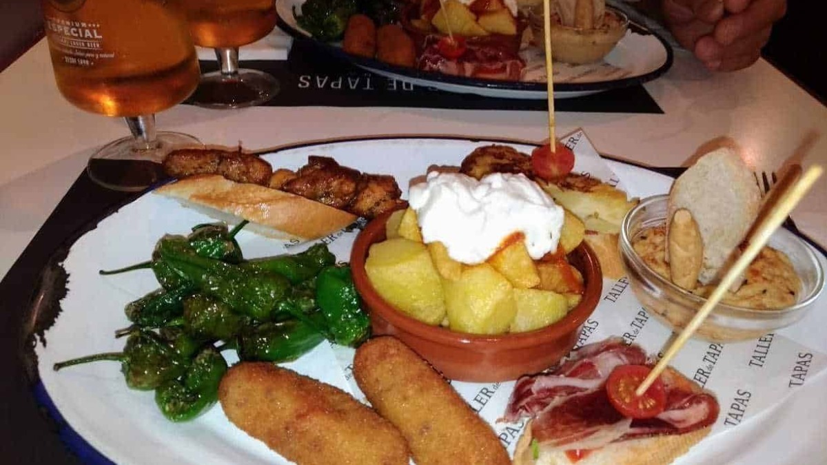 Extra large photo of a tradicional Spanish 'tapas' platter with potatoes, chorizo, peppers, ham and bread, served with two glasses of beer in a restaurant.
