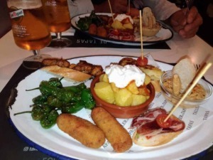 Extra large photo of a tradicional Spanish 'tapas' platter with potatoes, chorizo, peppers, ham and bread, served with two glasses of beer in a restaurant.