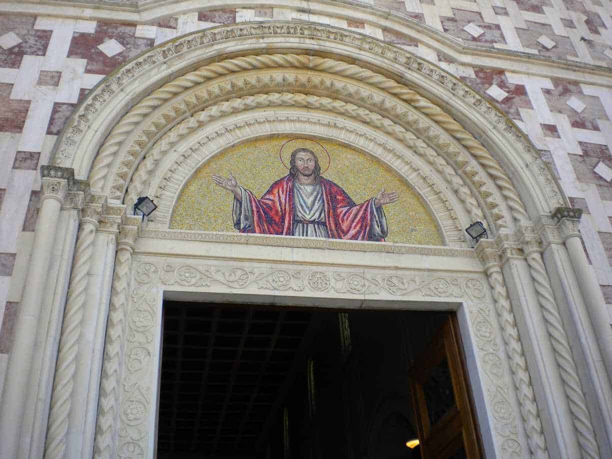 Manoppello in abruzzo: Altezza raffigurazione di Gesù Cristo sul portale di una chiesa in stile romanico, con dettagli in marmo scolpito e mosaico colorato alle spalle.