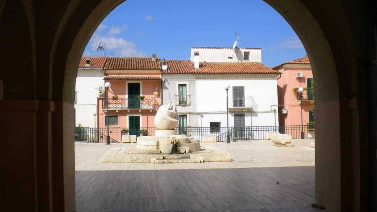 Villaggio di case colorate e piazza con fontana, vista attraverso un arco, in una tipica scena italiana.