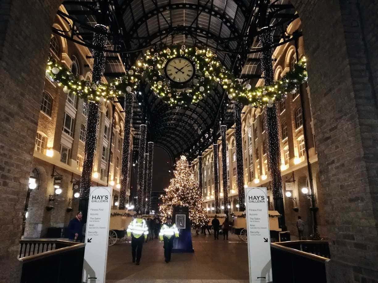 Quartieri da scoprire: Decorazioni natalizie all'interno di un centro commerciale con albero di Natale illuminato, ghirlande festive e luci scintillanti, creando un'atmosfera magica e accogliente durante il periodo delle feste.