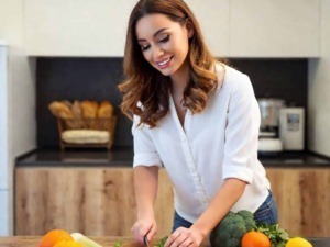 ArsnellALT: Donna che taglia verdure fresche sulla cucina moderna, con frutta e ortaggi di stagione sul tavolo, perfetta per contenuti di cucina salutare e ricette naturali.