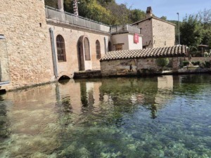 Vecchia centrale idroelettrica ristrutturata con pareti di mattoni e finestre ad arco, situata sul bordo di un lago naturale circondato da vegetazione.