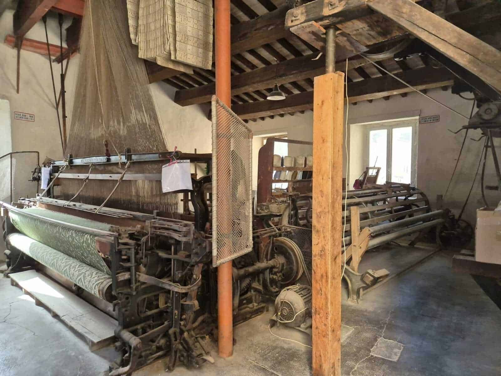 Macchina tessile vintage in un laboratorio artigianale con travi in legno e macchinari typici, ambientazione rustica, ideale per immagini di produzione tessile tradizionale, artigianato e storia industriale.