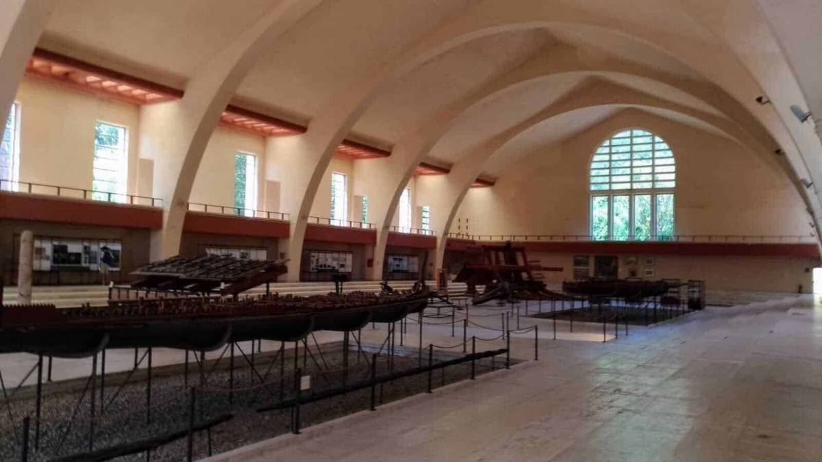 Antico museo con arcos a vela e grandi finestre, esposizione di barche storiche in legno e strumenti nautici, ambiente luminoso e spazioso, ideale per appassionati di storia marittima e architettura.
