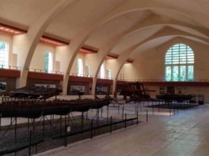 Antico museo con arcos a vela e grandi finestre, esposizione di barche storiche in legno e strumenti nautici, ambiente luminoso e spazioso, ideale per appassionati di storia marittima e architettura.