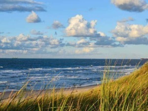 Spiaggia con dune di sabbia, mare blu e nuvole bianche in un cielo sereno, ideale per vacanze e relax estivo in Italia.