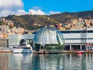 Sfera di vetro moderna sul porto di Genova con yacht ancorati e vista sui colli urbani circostanti.