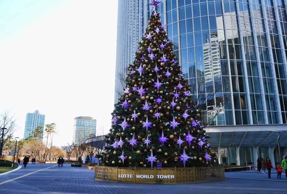 Albero di Natale decorato con luci viola e palline dorate davanti a un grattacielo moderno a Lotte World Tower, Seoul. Perfetto per il periodo natalizio in città dinamiche e futuristiche.