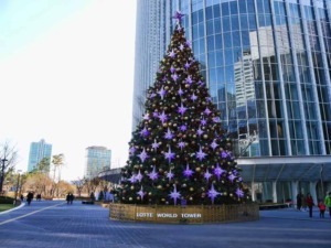 Albero di Natale decorato con luci viola e palline dorate davanti a un grattacielo moderno a Lotte World Tower, Seoul. Perfetto per il periodo natalizio in città dinamiche e futuristiche.