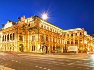 Immagine di un elegante teatro storico di Vienna, illuminato di sera con luci calde, che evidenziano la sua architettura neoclassica e rinascimentale.
