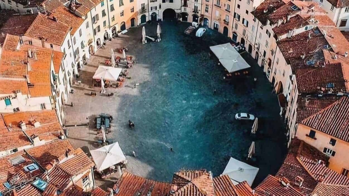 Vicolo circolare di case con tetti in terracotta e una piazza centrale con bar e tavoli, in un suggestivo borgo italiano, perfetto per foto di viaggi e turismo.
