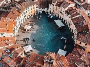 Vicolo circolare di case con tetti in terracotta e una piazza centrale con bar e tavoli, in un suggestivo borgo italiano, perfetto per foto di viaggi e turismo.