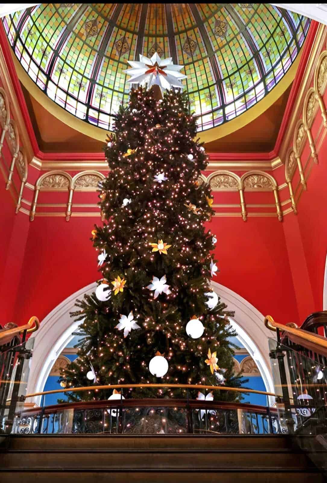 Albero di Natale decorato con luci e ornamenti sotto una cupola di vetro colorata in un salone elegante.