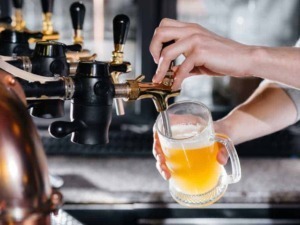 Birra artigianale versata da un rubinetto in un pub, focus su produzione di birra, stile artigianale e atmosfera accogliente.