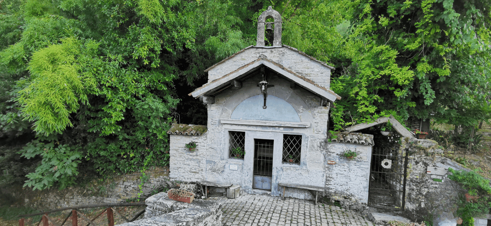 Portico di Romagna il paese di Dante e Beatrice 5 Piccola cappella in pietra con affreschi e fiorellini, circondata da alberi verdi, rivelando un’atmosfera di serenità e spiritualità in un contesto naturale.