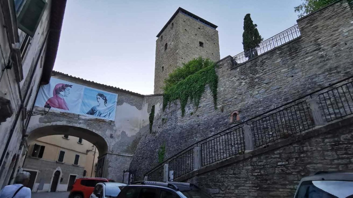 Castello storico con torre medievale e archi in pietra, situato in un suggestivo borgo italiano, decorato con una bandiera colorata e affascinante architettura antica.