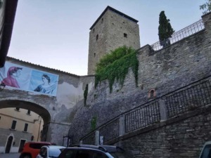 Castello storico con torre medievale e archi in pietra, situato in un suggestivo borgo italiano, decorato con una bandiera colorata e affascinante architettura antica.