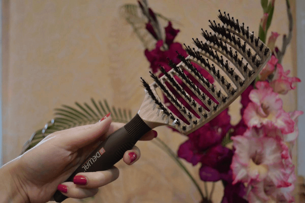 Pettine per capelli con denti robusti in plastica e cuscinetti in gomma, utilizzato per acconciature e cura dei capelli, con sfondo di fiori rosa e tropicali, ideale per tutorial di hairstyling.